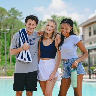Three students in front of a pool smile at the camera