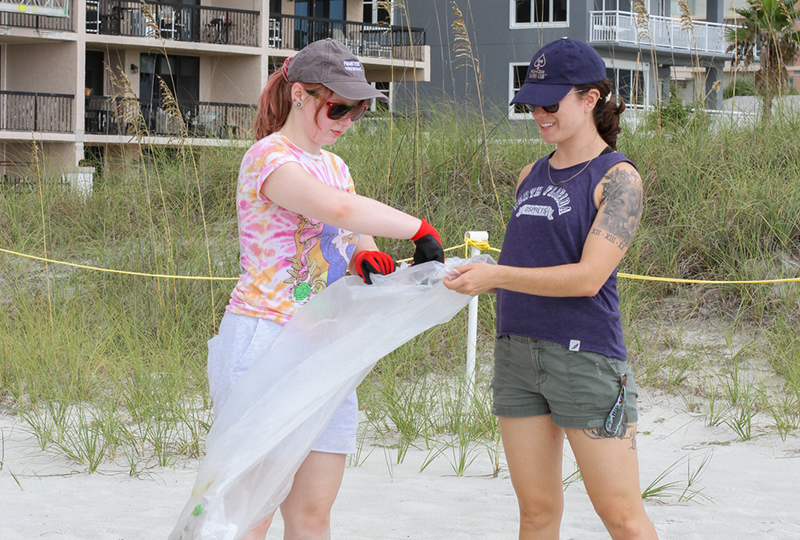 two students cleaning up garbage from the beach
