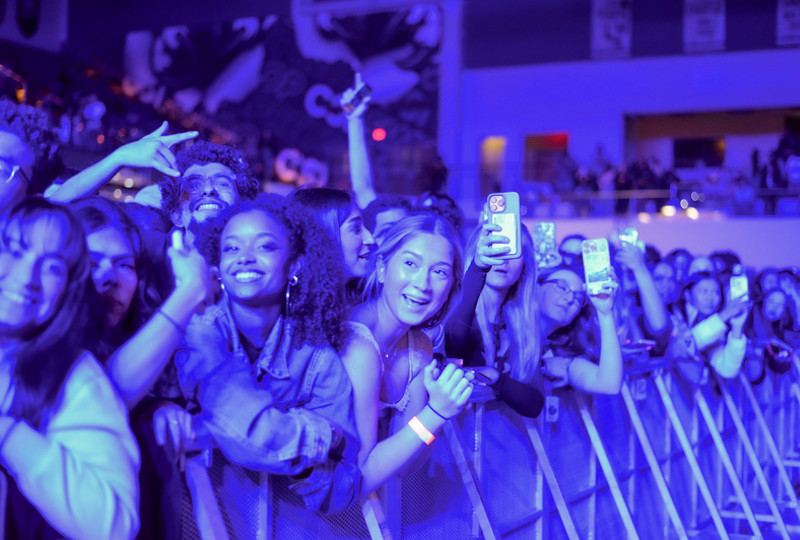 Students in a crowd watching a concert and filming on their phone