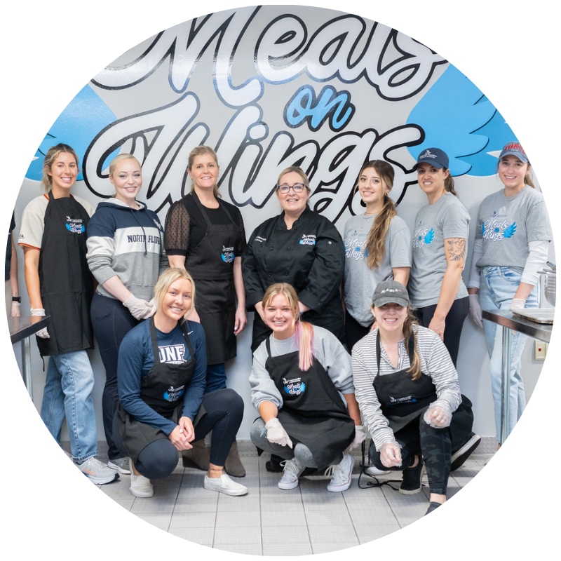 meals on wings group picture in front of mow logo on the wall