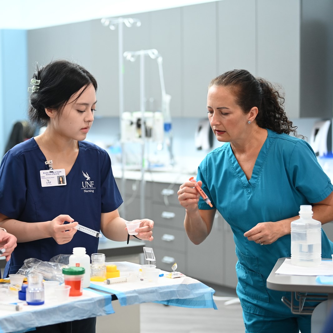 Nursing faculty with a nursing student instructing on piping technique
