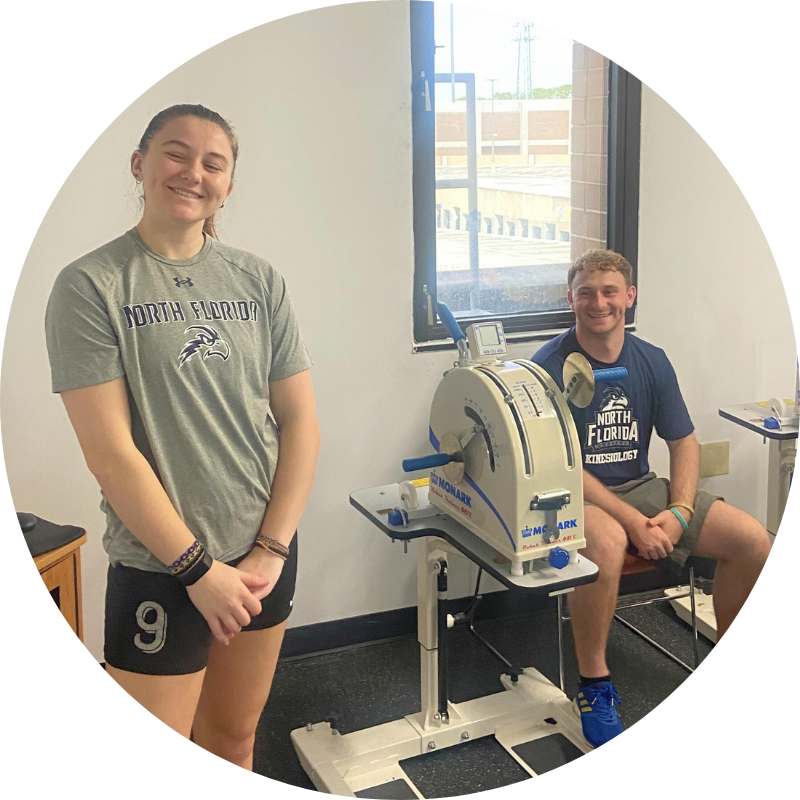 two kinesiology students smiling. one standing, one sitting