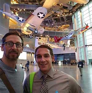 two men in a museum with an airplane in the background