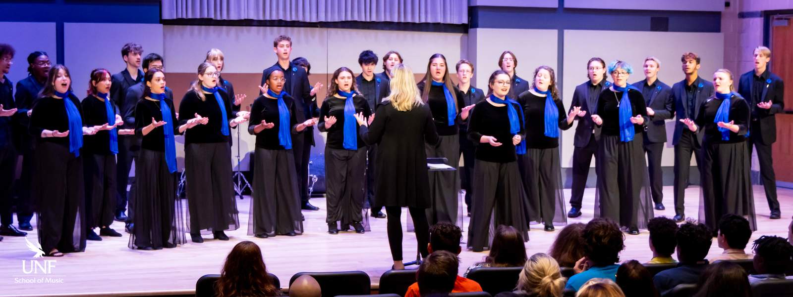 Singers on stage wearing black with blue stoles. 