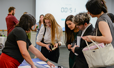 Five individuals standing around a table talking.