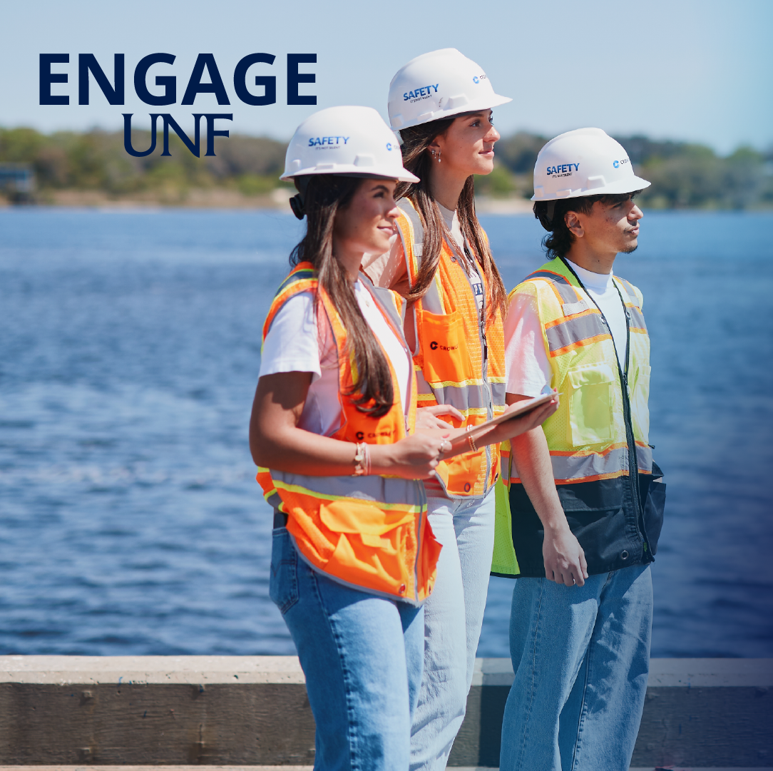 Three students in hard hats at a port with the water behind them.