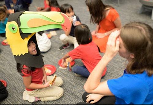 Honors students host a Halloween party with elementary students child has on a toucan head piece