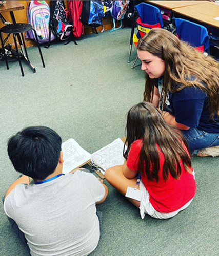 UNF student in PREP sitting on the floor and reading with two elementary students.