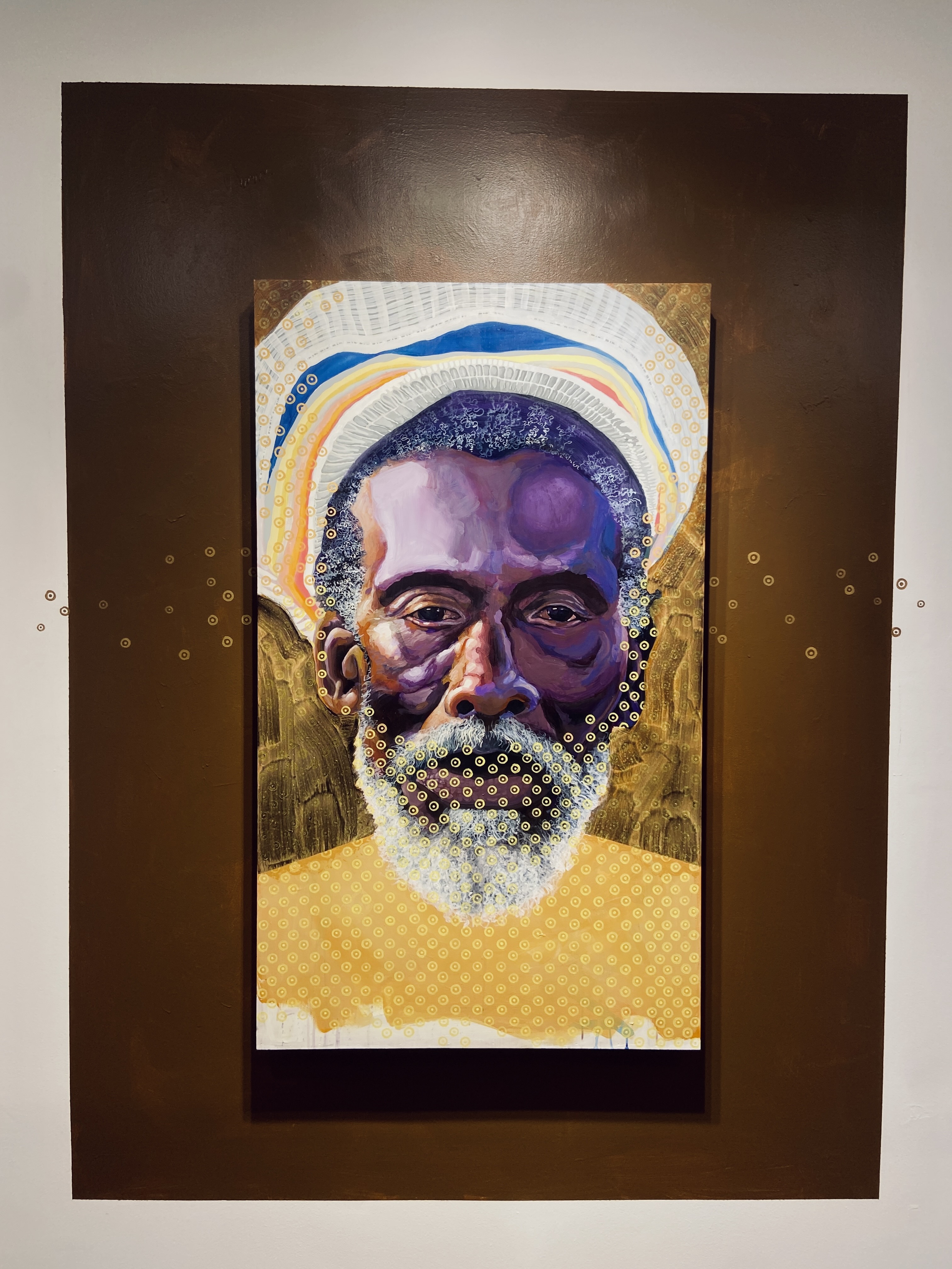 A vibrant portrait of an elderly man with a beard, featuring rich colors and intricate patterns in the background. The artwork showcases cultural themes and artistic depth.