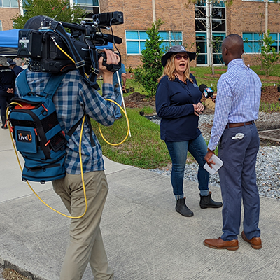 Camera man filming reporter interview woman in hat outside UNF building
