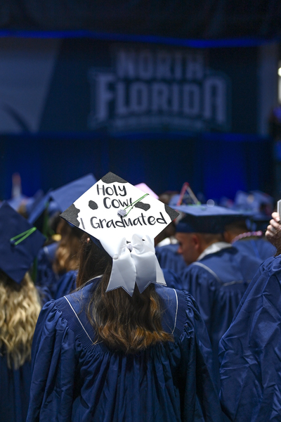 UNF grad in cap and gown with a sign on the cap