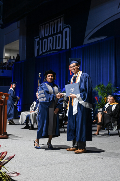 UNF student on stage at graduation holding his diploma