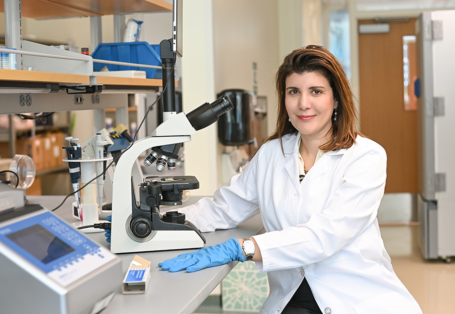 Alya Limayem posed next to a microscope in her white coat