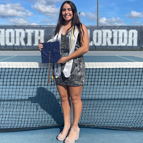 ana paula holding her grad cap on the UNF tennis courts