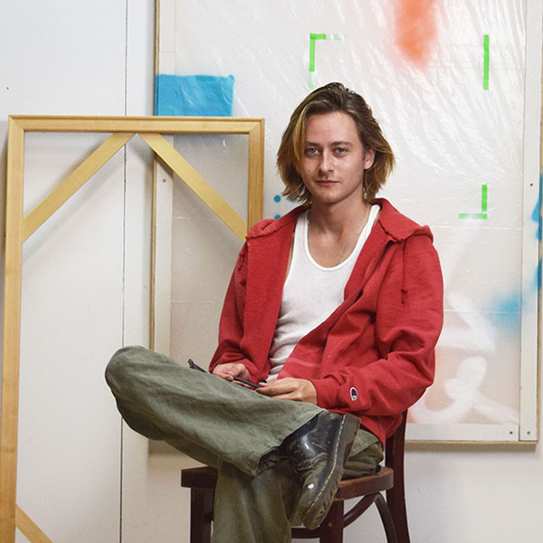 Brennan Wojtyla sitting in chair in front of a canvas