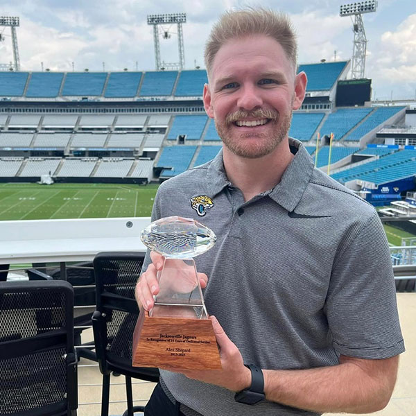 alex standing in the jags stadium holding up a trophy