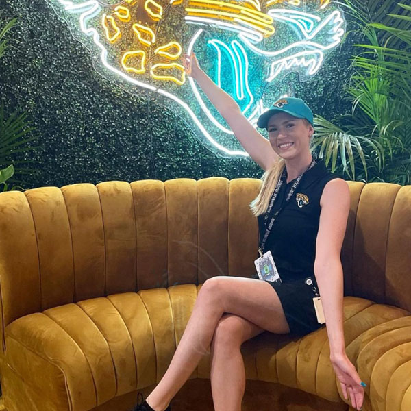 kristen in her jags gear in front of a neon cat sign 