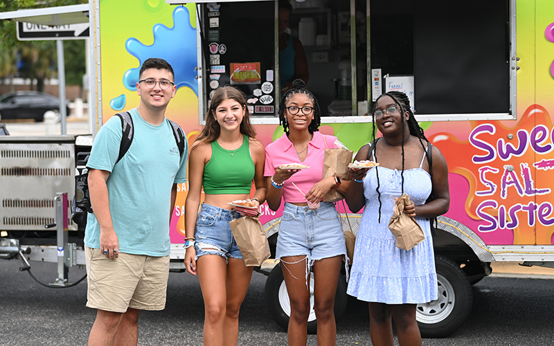 four students in front of a food truck with funnel cakes
